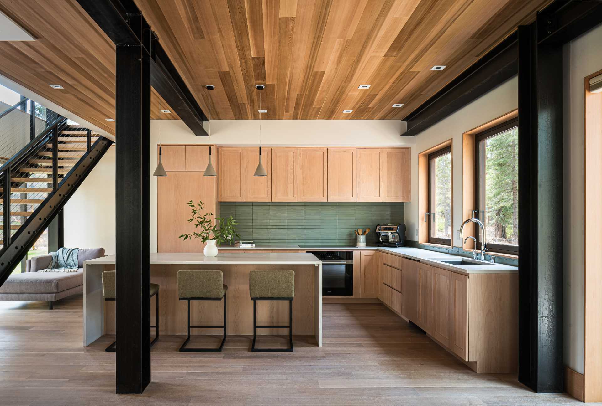 This modern kitchen has a wood ceiling, light wood cabinets, and a green tile backsplash.