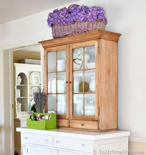 Fake purple hydrangea flowers on top of a glass fronted cabinet