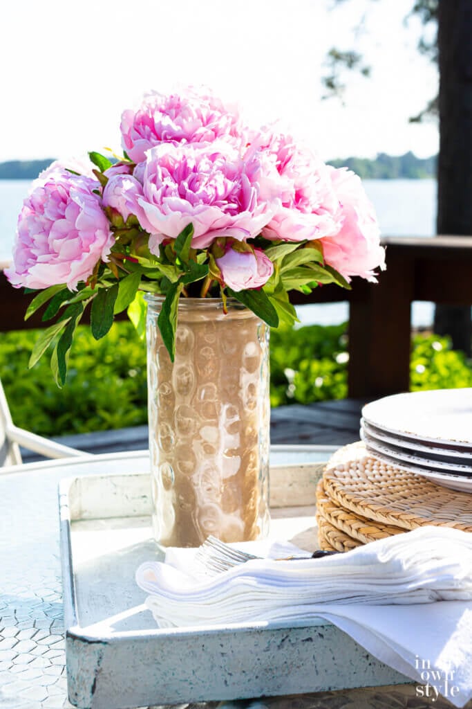 Tall glass vase on deck by lake changed to be a colorful glass vase to hold flowers.