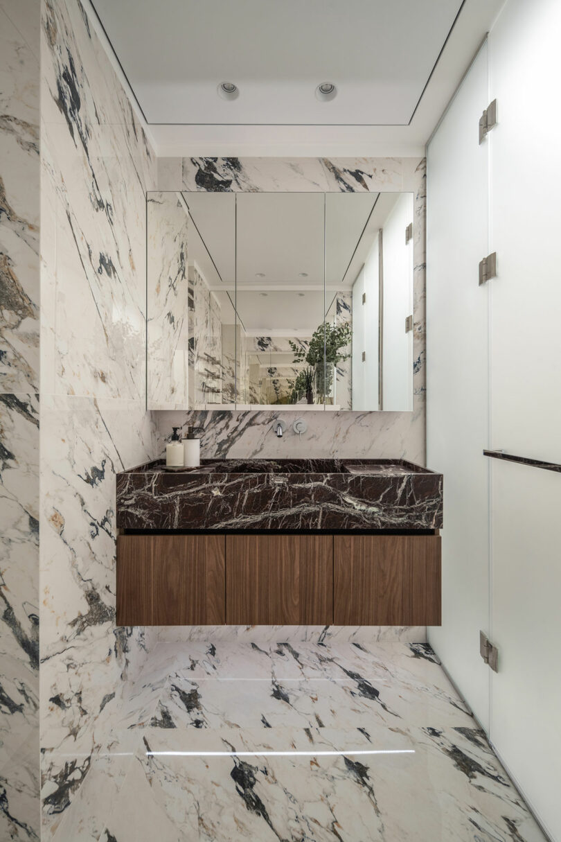 Bathroom with white and black marble walls and floor, a wooden vanity with a dark marble countertop, large mirror, and frosted glass doors.