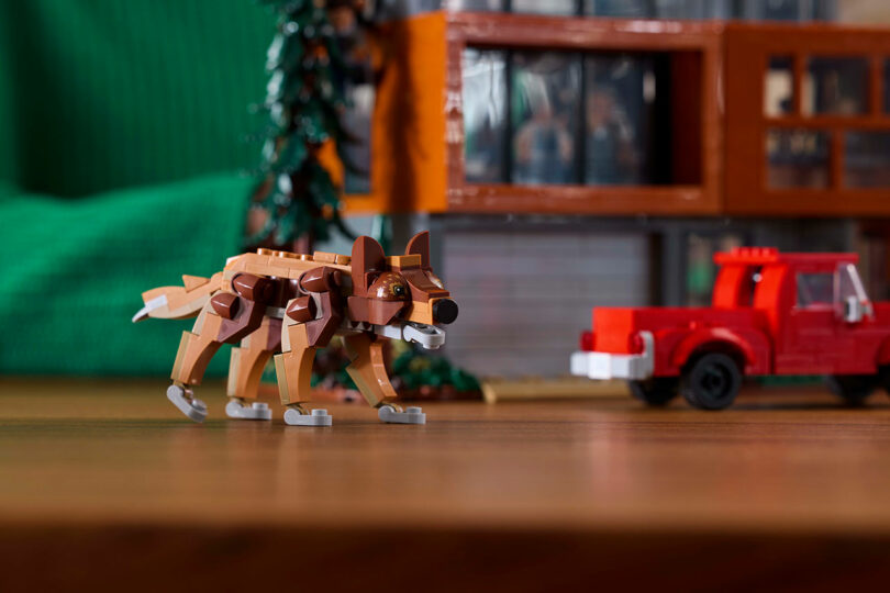 A Lego wolf model stands on a wooden surface in front of a red Lego truck and a Lego tree.