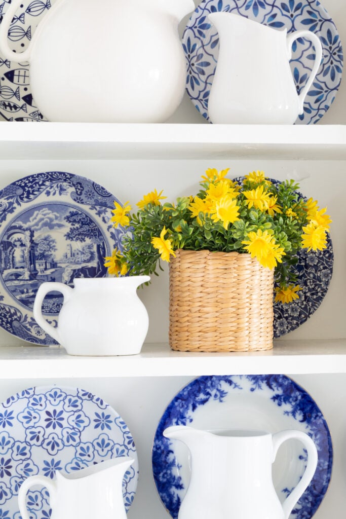 Spring flowers in a wicker vase displayed on open shelves in a white kitchen.