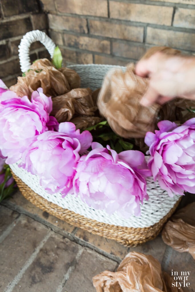 Stuffing a large basket with balled up plastic bags to fill it before placing faux flowers in.