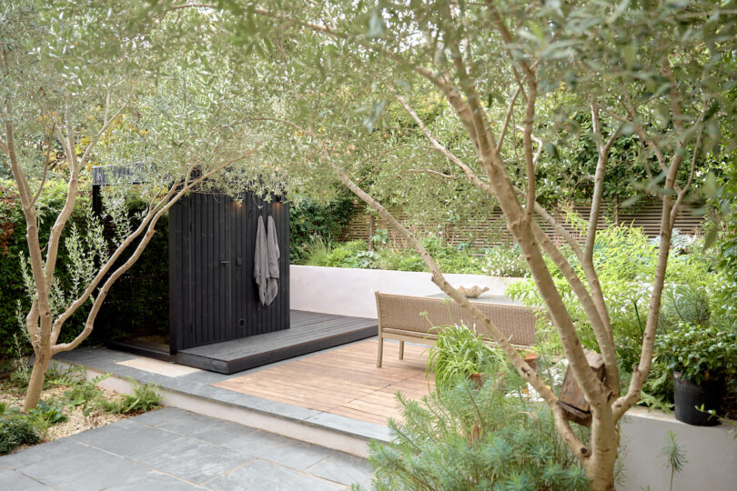 Garden with trees and plants, a wooden deck, outdoor furniture, and a black outdoor sauna