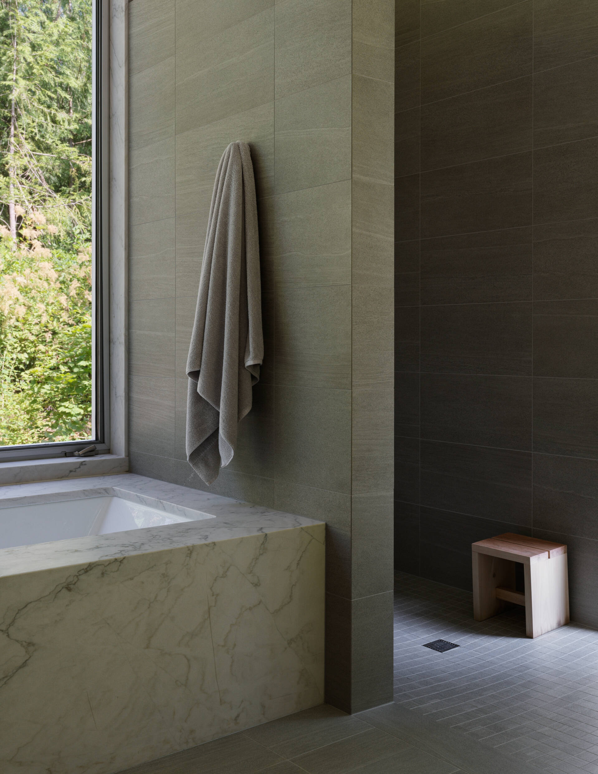 In the primary bath, impervious tile meets natural light in a calm, refined composition. A built-in bathtub offers a peaceful spot to unwind while looking out to the trees beyond.