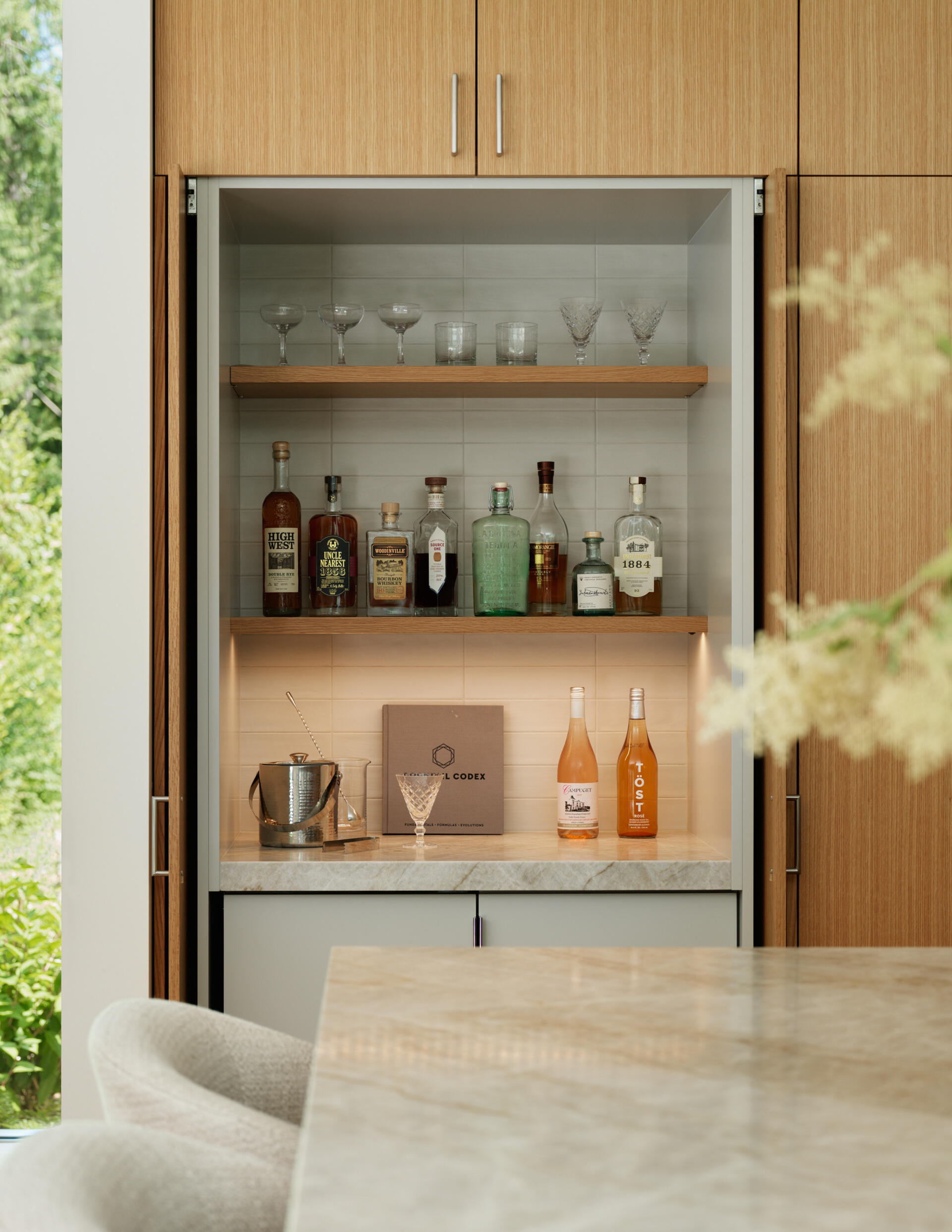 Within the kitchen’s clean-lined design lies a subtle surprise, a hidden bar tucked within the seamlessly integrated cabinetry. Designed for both function and discretion, the bar offers a dedicated space for cocktails without interrupting the kitchen’s minimalist aesthetic.