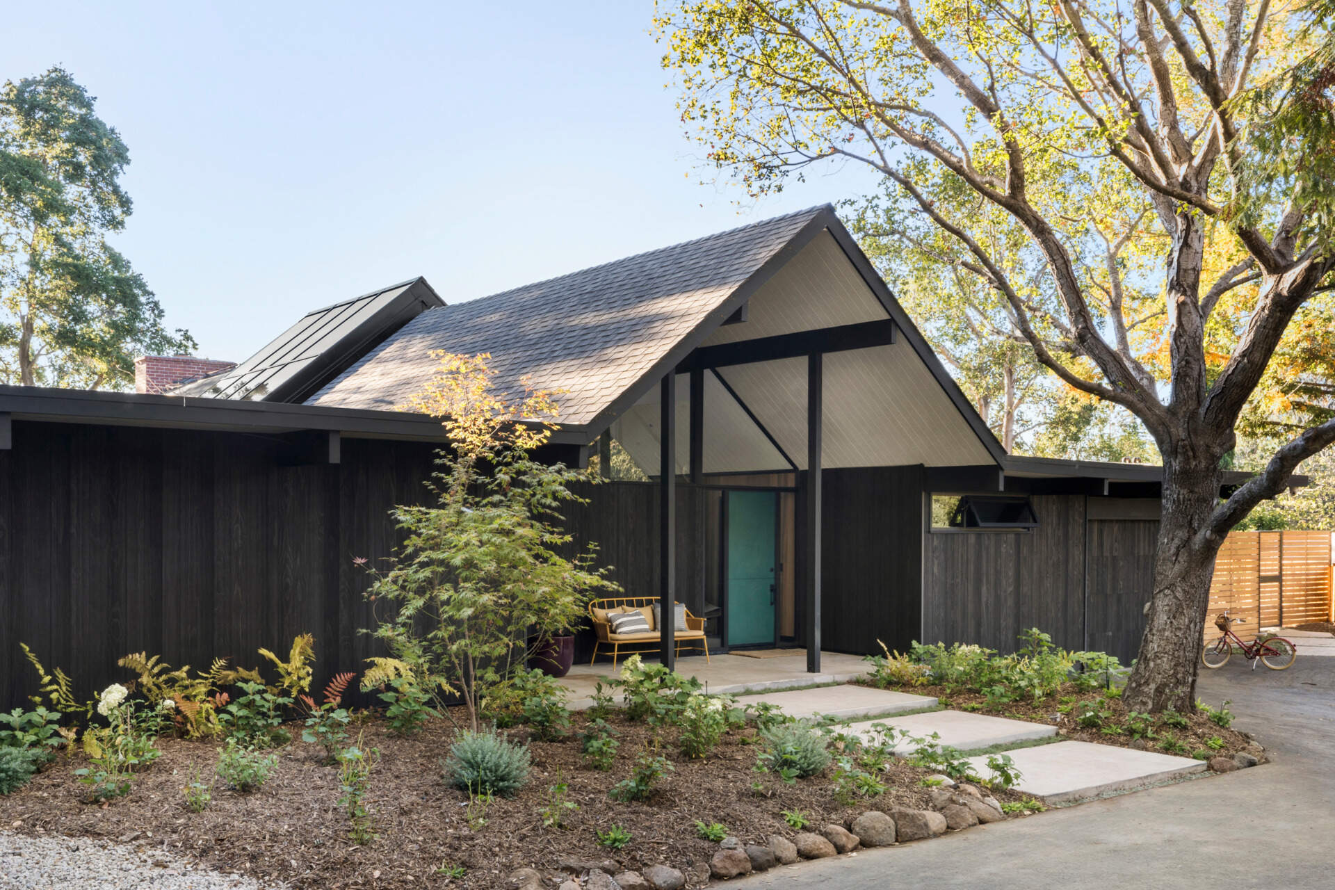 Set back from the street and accessed via a long driveway, the residence combines privacy with striking form. Its exterior has been updated using Shou Sugi Ban Accoya barn wood siding, adding texture and durability. A central gabled roof defines the structure, flanked by two flat-roofed wings that retain the home's mid-century profile.