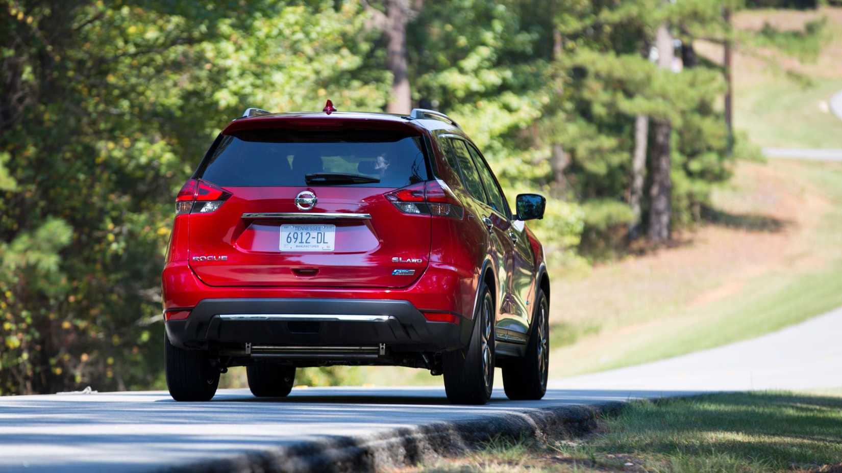 Dynamic rear 3/4 shot of a red 2017 Nissan Rogue Hybrid driving on a road lined by trees.