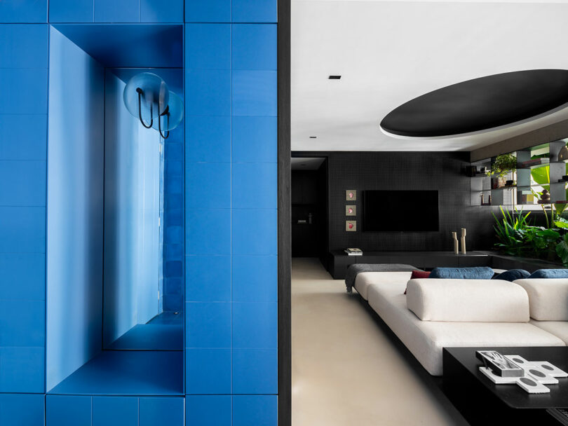 Modern living room with a blue-tiled wall feature, white sectional sofa, black accent wall, and indoor plants.