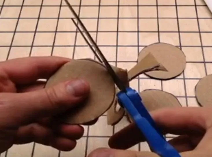 Person cutting cardboard shapes with scissors on a grid-patterned surface.