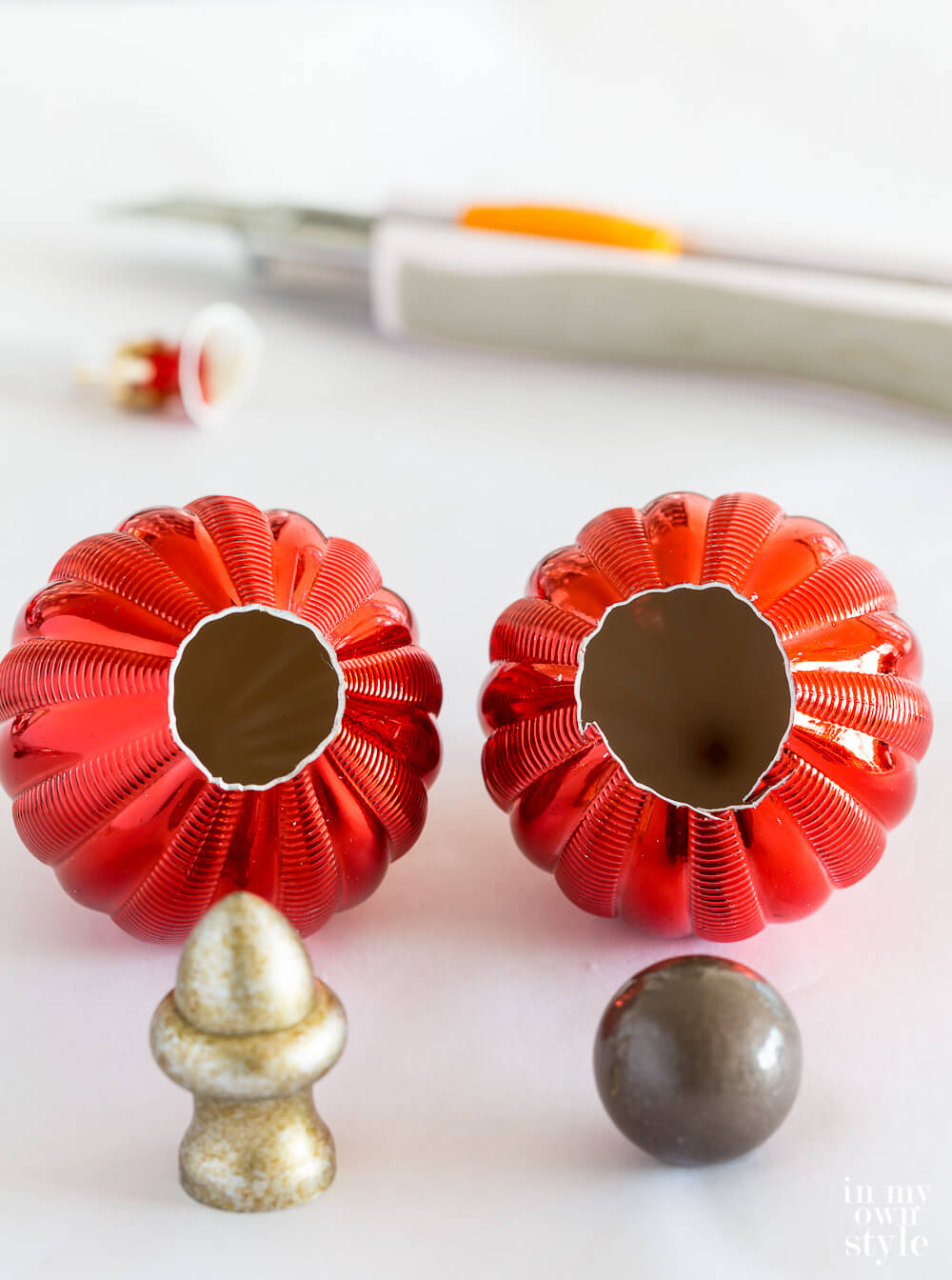 Two cut shatterproof ornaments and two lamp finials on a worktable.