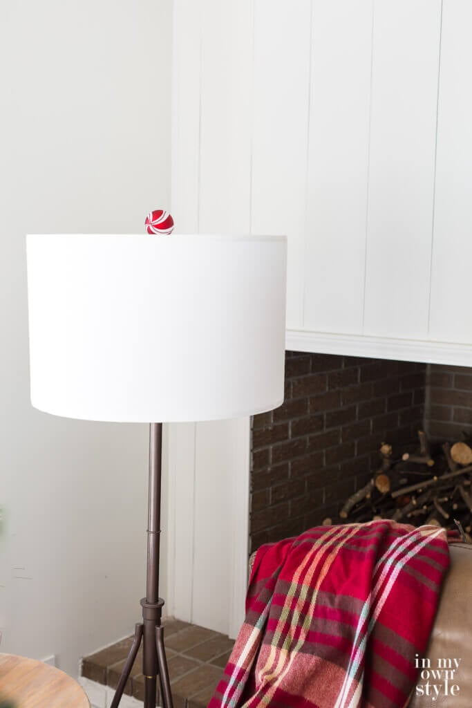 Bronze floor lamp with white drum shade with a red and white Christmas ornament finial.