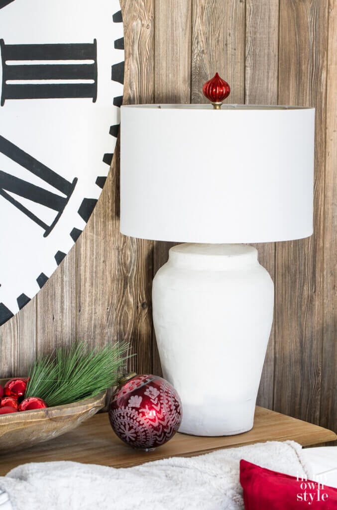 Holiday lamp finial idea. Close up of white table lamp with red Christmas ball ornament made into a finial above the lamp shade.