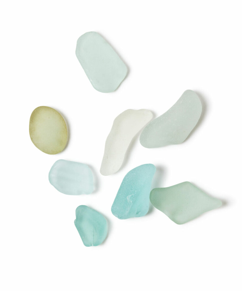 Assorted pieces of sea glass in shades of blue, green, white, and yellow displayed on a white background, inspired by the coastal aesthetics of Brent Buck.